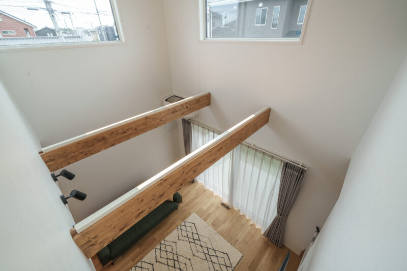 吹き抜けを2階から見たところ。梁の上部には「梁の上のせたろう」という間接照明を設置。夜は吹き抜けを優しく照らしてくれる。上部のFIX窓は、夏の太陽光で暑くならないように、光は通し熱を遮る日射遮蔽型を採用。「軒を出して日射を遮るという方法もあるのですが、外観デザインを優先しました」とご主人。<br />
